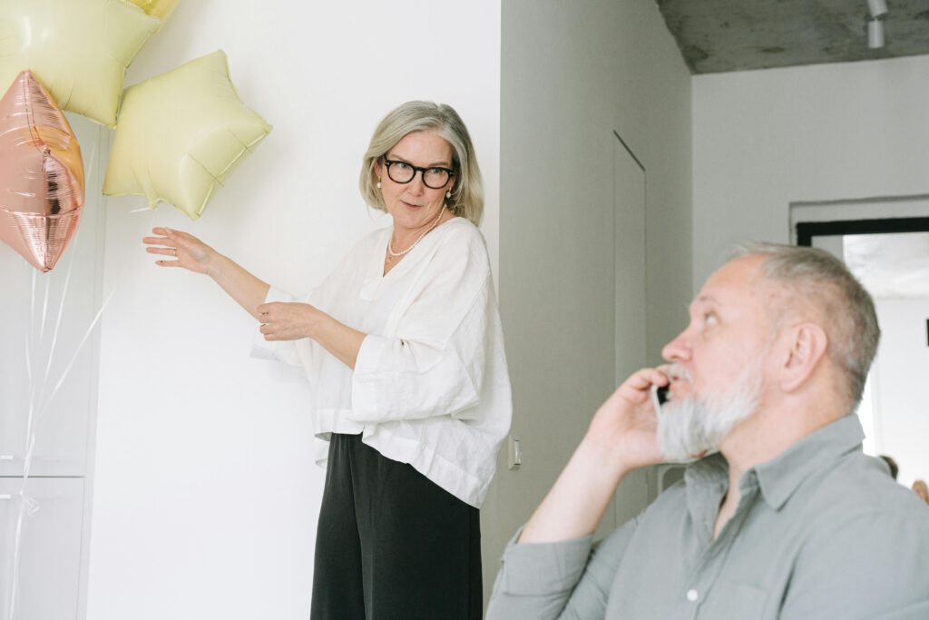 An elderly couple celebrates indoors with bright balloons and a phone call.